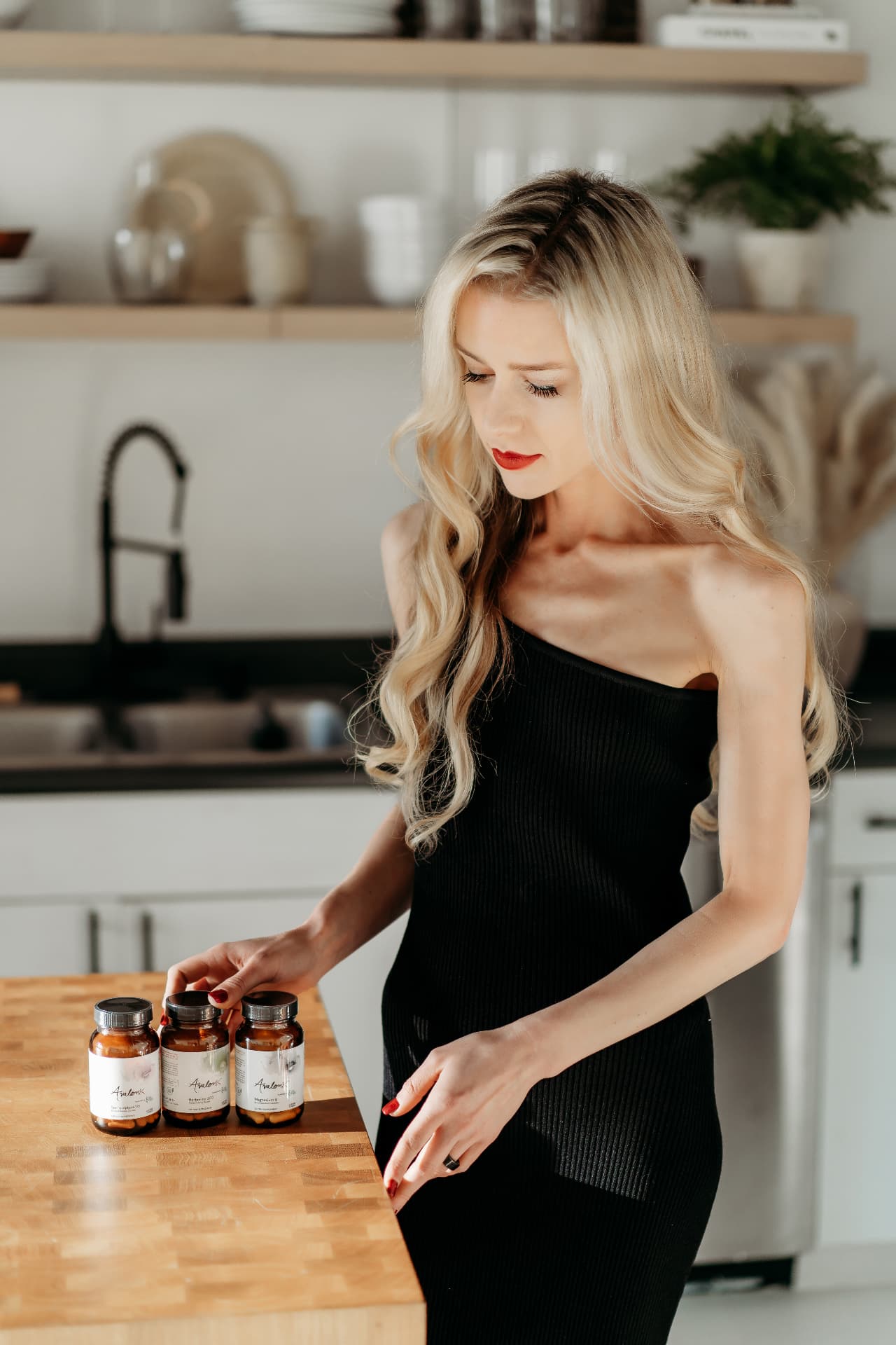 Melanie Avalon in a kitchen looking at AvalonX supplement bottles on the counter