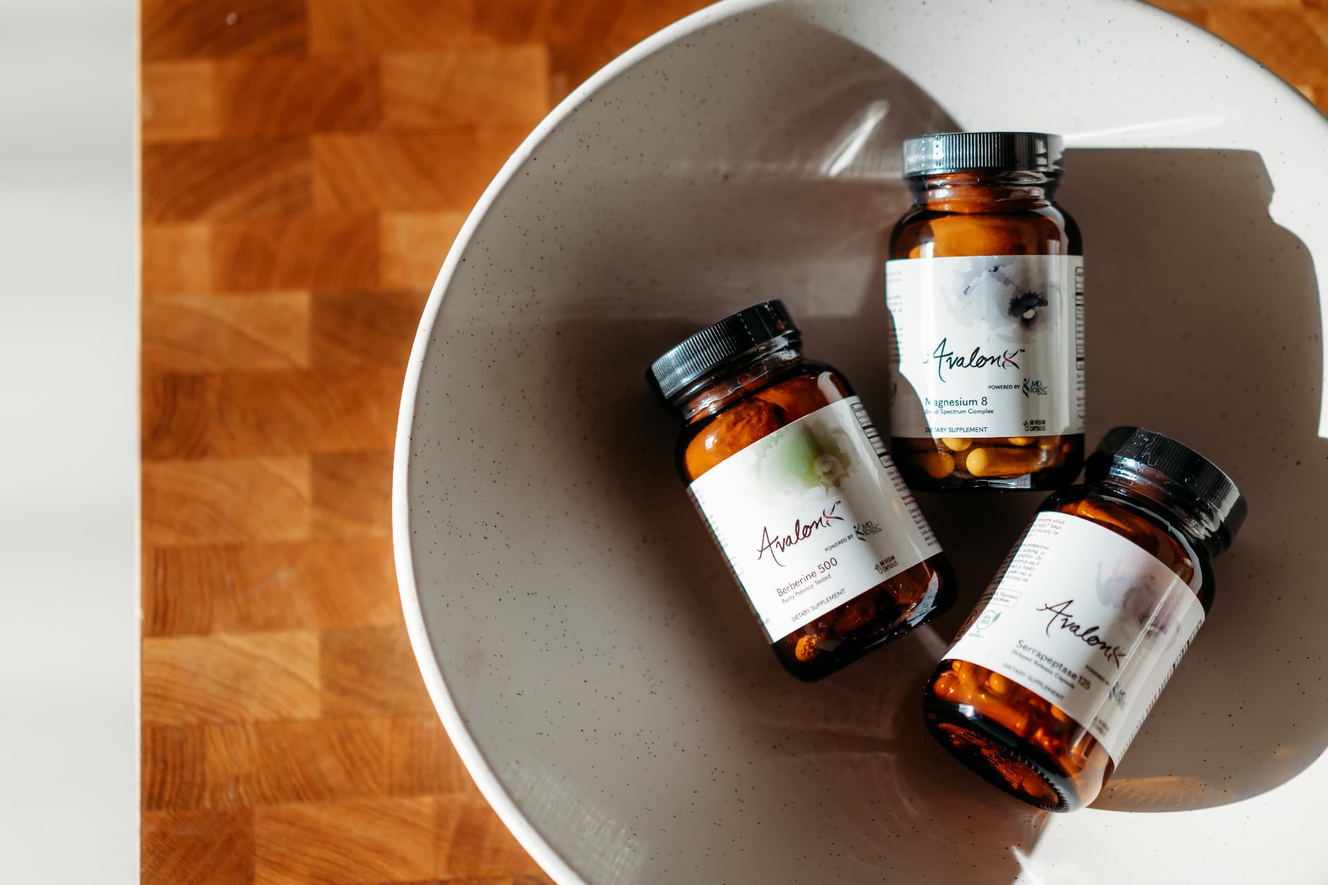 AvalonX supplement bottles arranged in a white bowl on a wooden surface